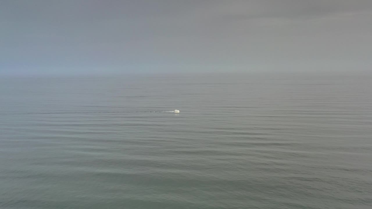 Small floating object farther right on calm water with gray sky above.