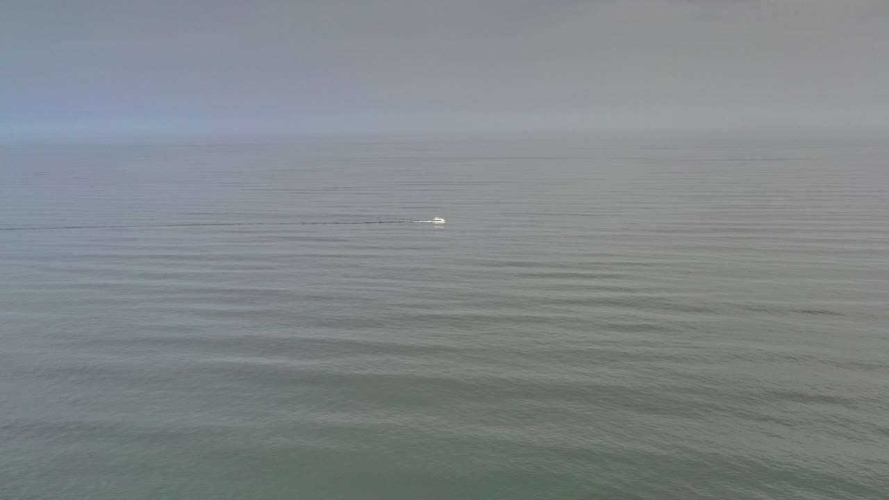 Wide ocean horizon with a small white boat on calm water.