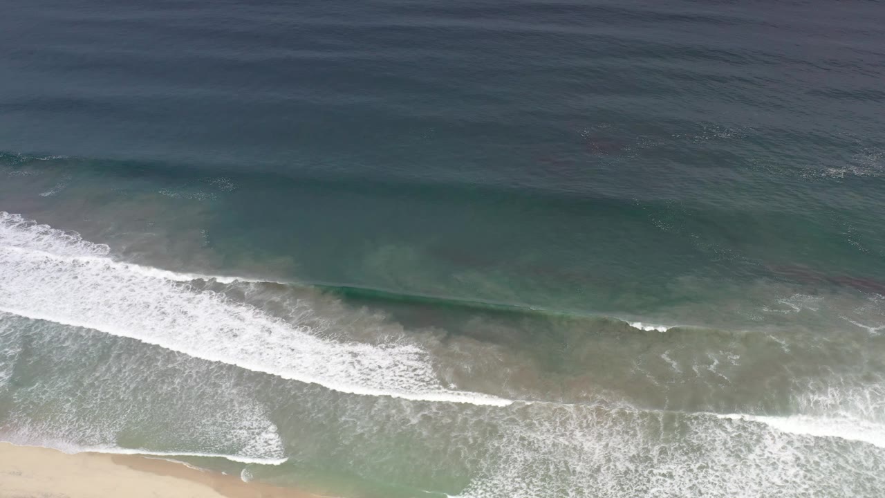 White surf line spreading across shallow green water near sand.