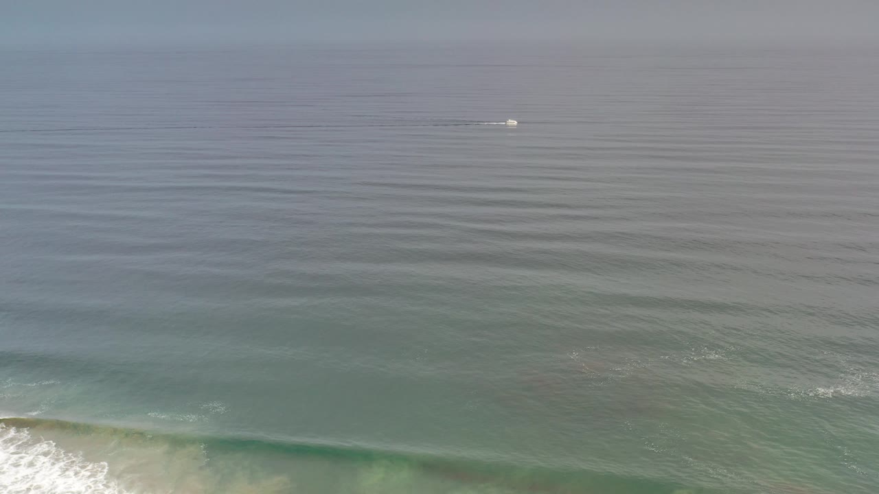 Calm ocean water with small surf and a distant white boat.