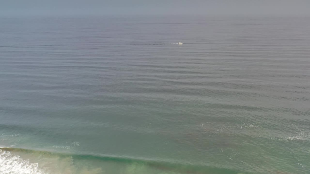 Los Cabos sea view with blue green water bands, light surf entering along the bottom, a small white boat farther offshore, and no visible people.