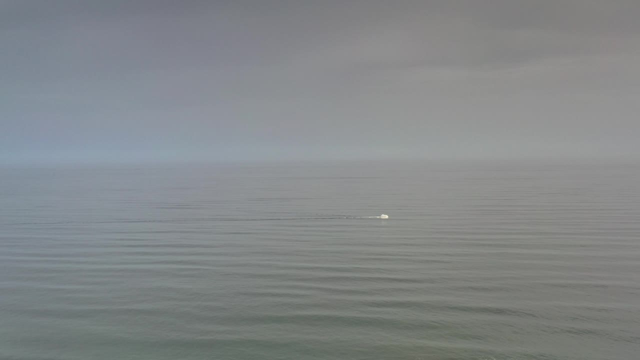 Overcast ocean view with faint ripples and a small white object near the horizon.