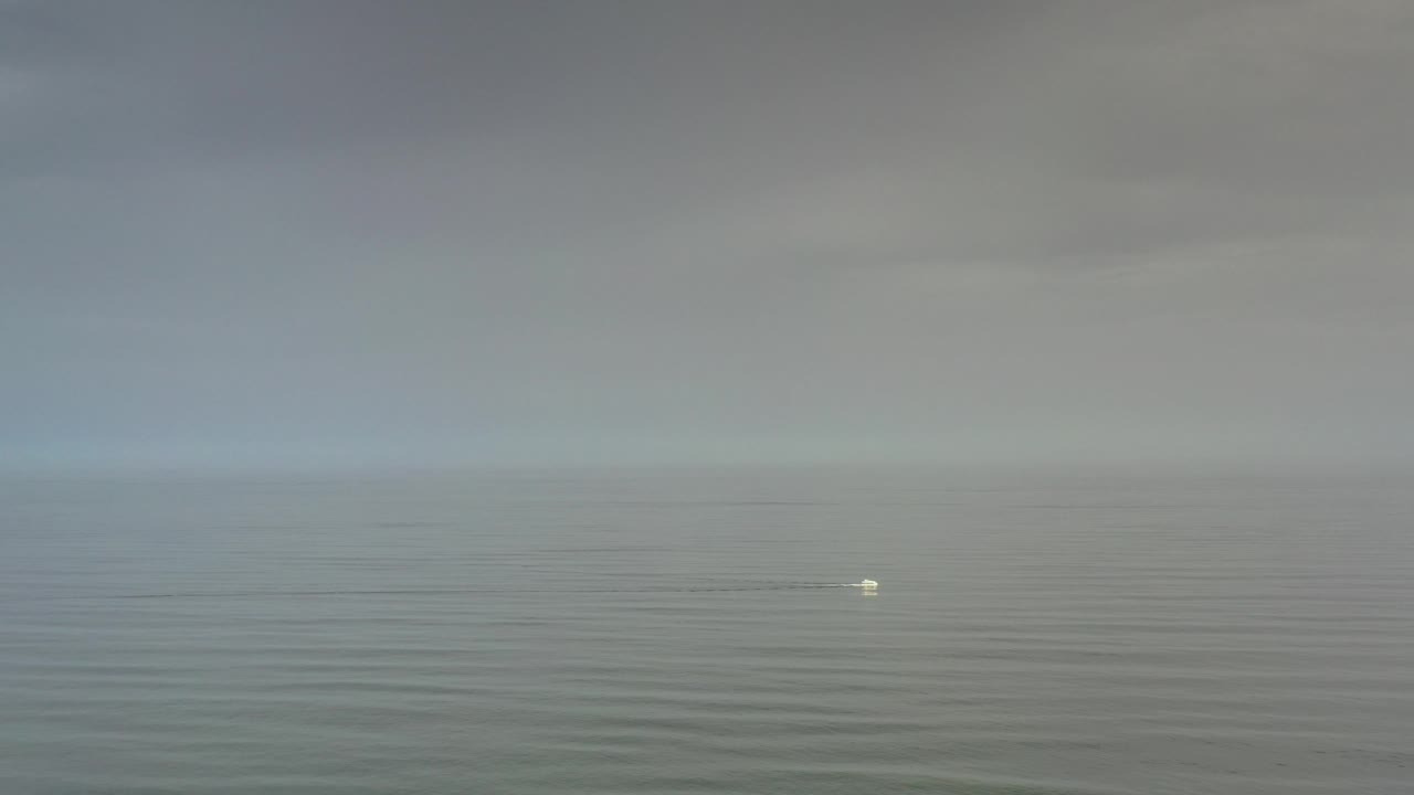 Muted ocean and gray sky with a small bright speck farther right on the water.