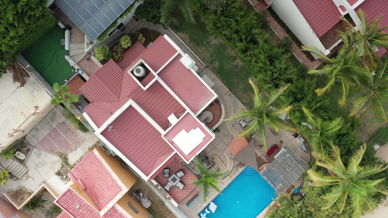 Aerial view of red-roofed residence, patio, palms, and bright pool.