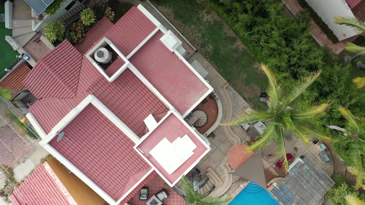Top-down view of a red-roofed house beside palms and patio paving.