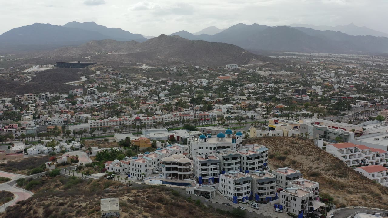 Aerial city view with hillside buildings and mountains in the distance.