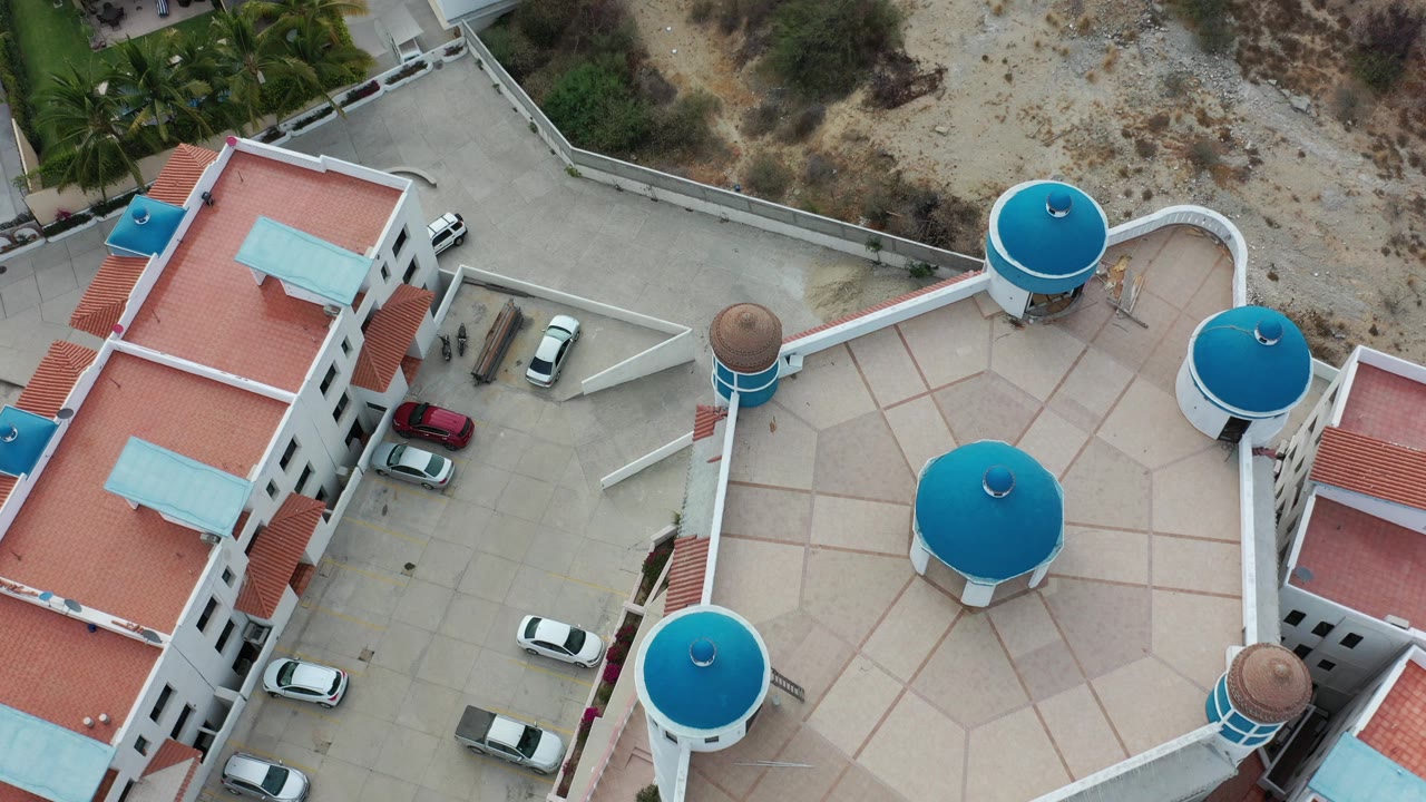 Overhead view of white buildings with red roofs, blue round rooftops, paved drives, and parked cars.