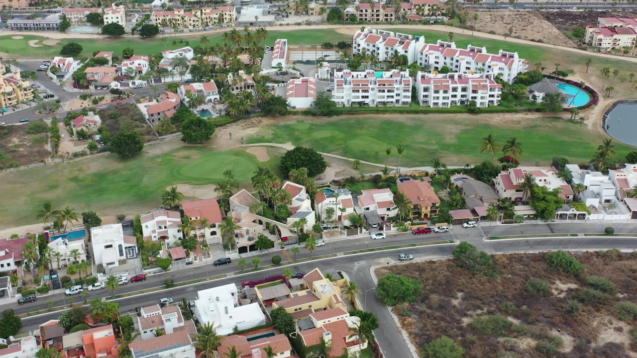 Aerial view of homes, a road, parked cars, and green fairway landscaping.