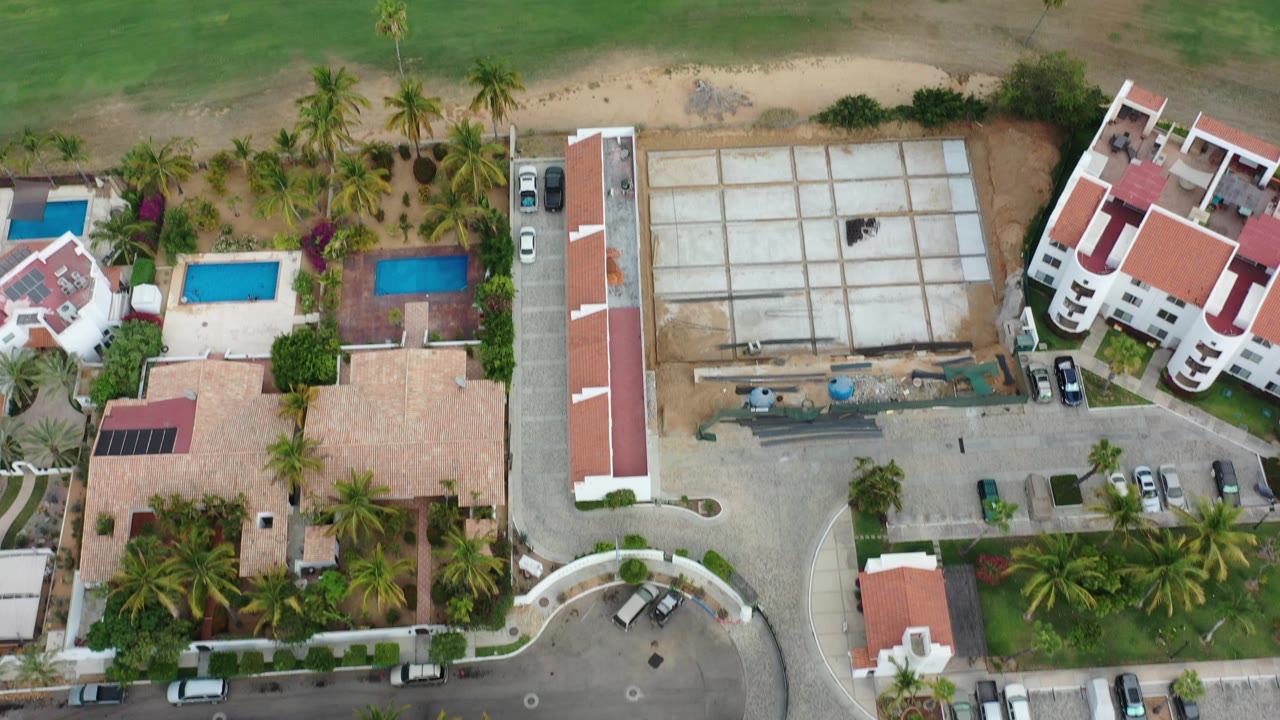 Overhead view of golf course, homes, pools, palms, and parked cars.