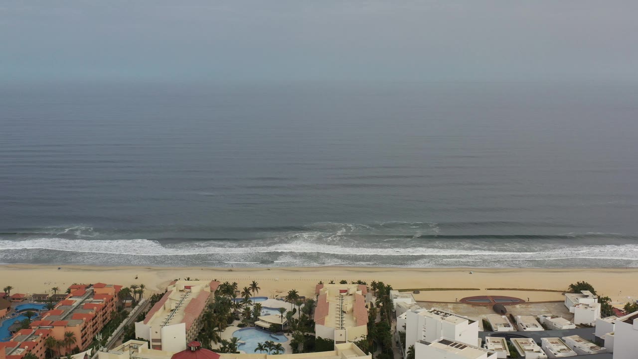 Aerial view of ocean waves, sandy beach, and beachfront buildings.