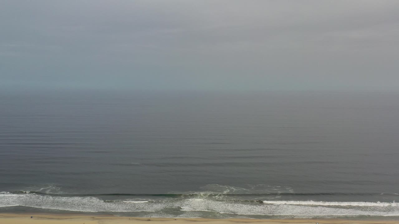 Gray ocean and surf along a narrow beach under misty sky