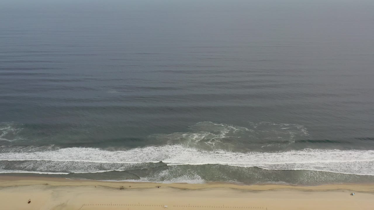 Overhead view of ocean waves reaching a sandy beach.
