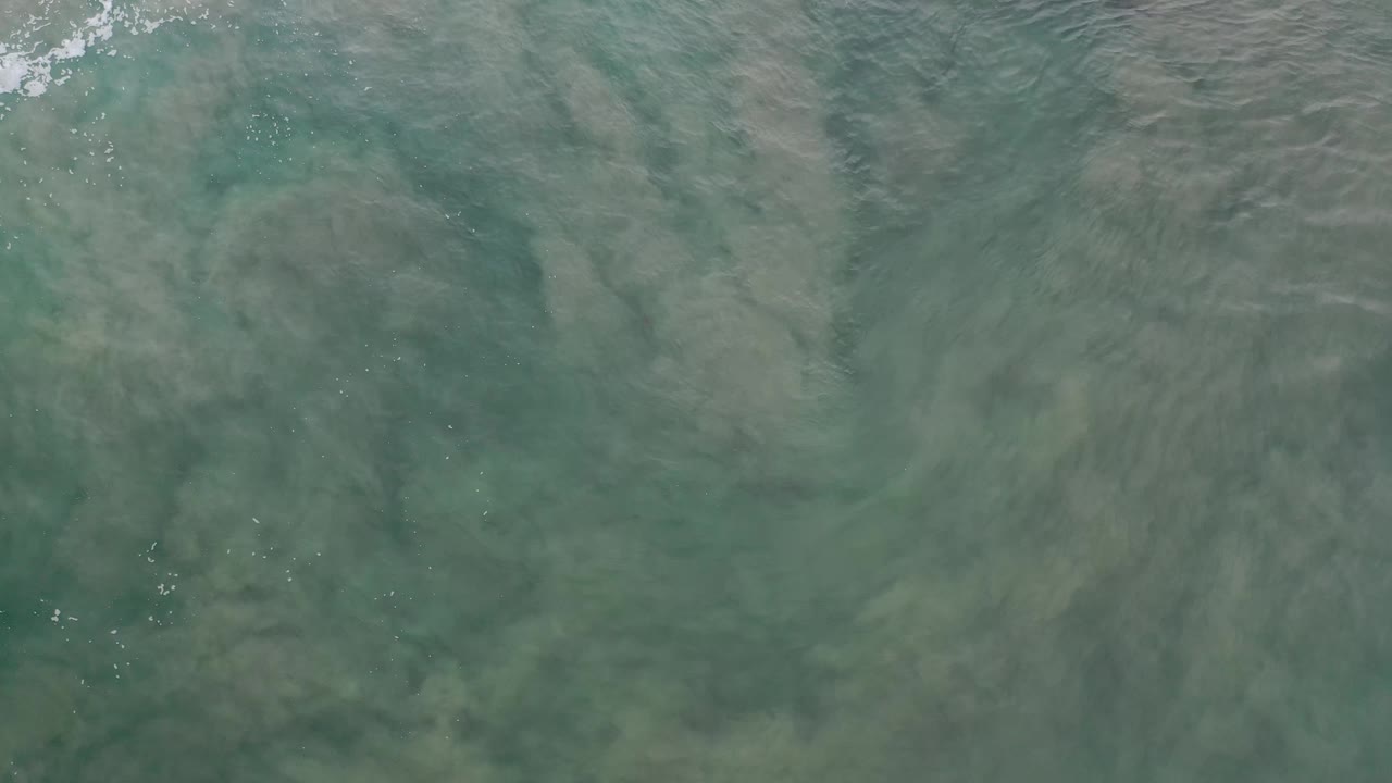 Green-blue shallow water in Los Cabos, Mexico, with cloudy sediment patterns under the surface and no visible people.