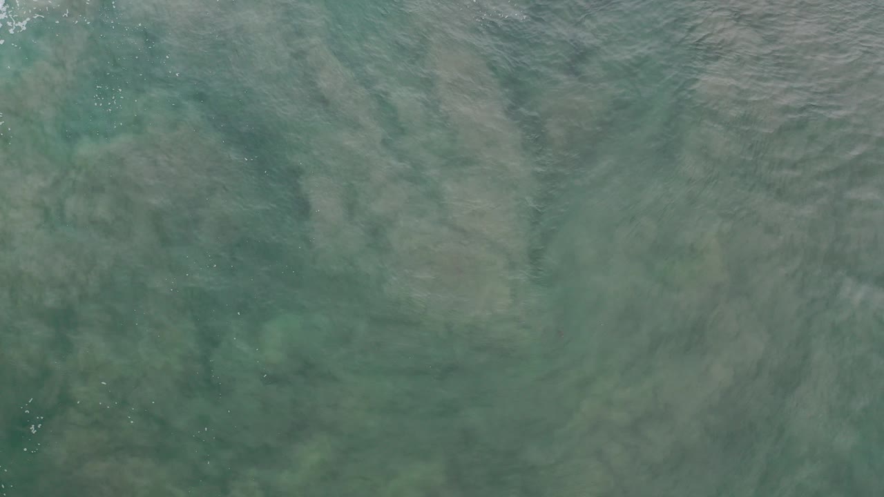 Overhead view of teal ocean water in Los Cabos, Mexico, with pale wave streaks across the surface and no visible people.