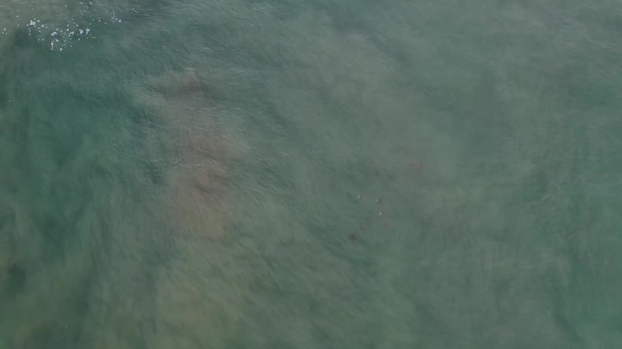 Aerial Los Cabos water surface with muted turquoise color, darker underwater streaks, and no visible people.