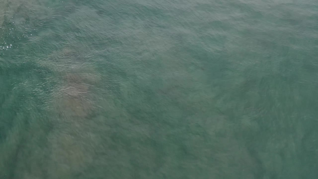 Green-blue Los Cabos water fills the frame, with darker underwater shapes softened by surface ripple, no visible people.