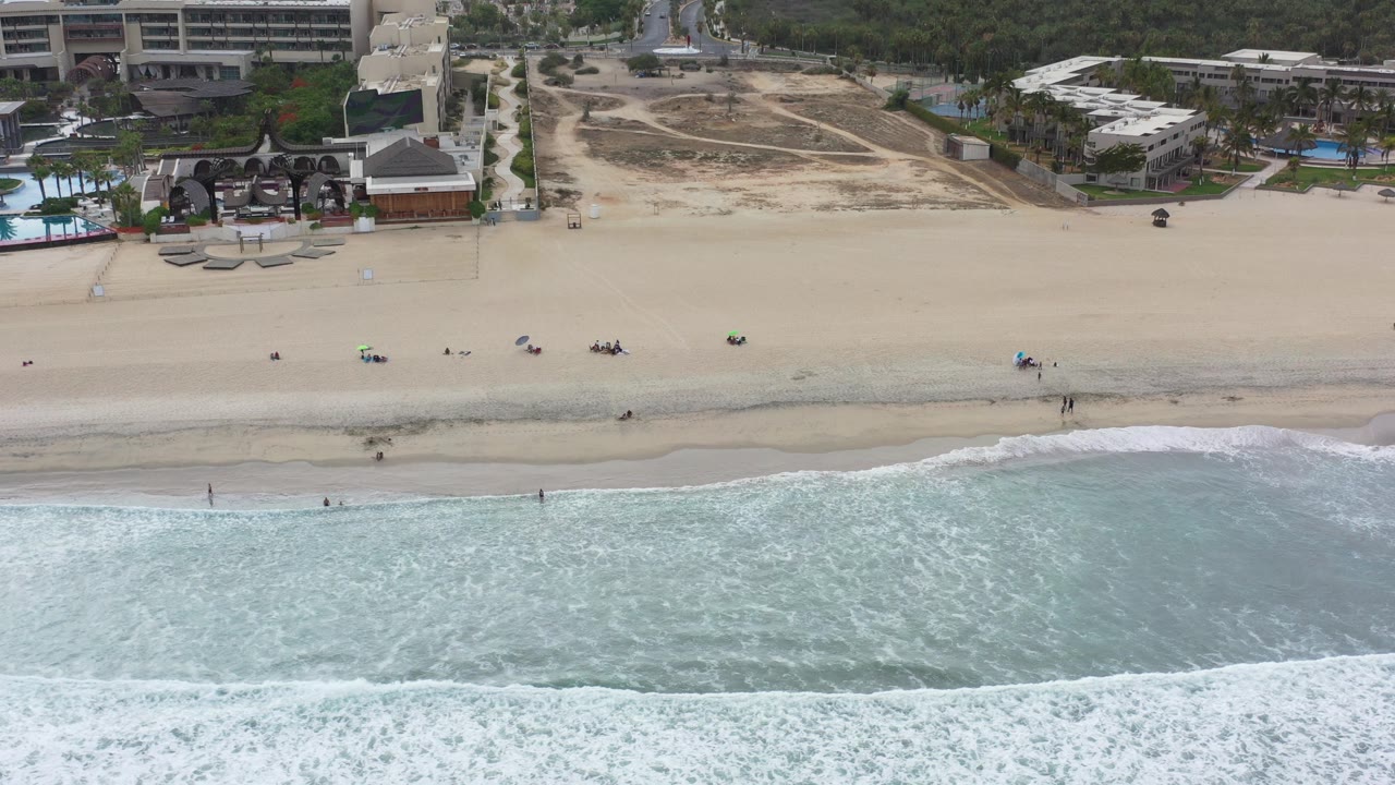 Overhead beach view with surf, sand, and oceanfront buildings.