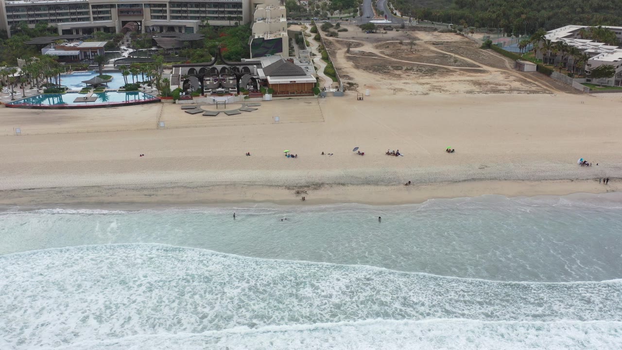Aerial view of surf, sand, pool area, and resort buildings.