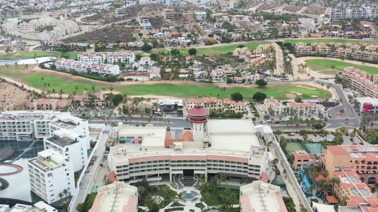 Aerial view of a curved resort building beside a golf course and roads.