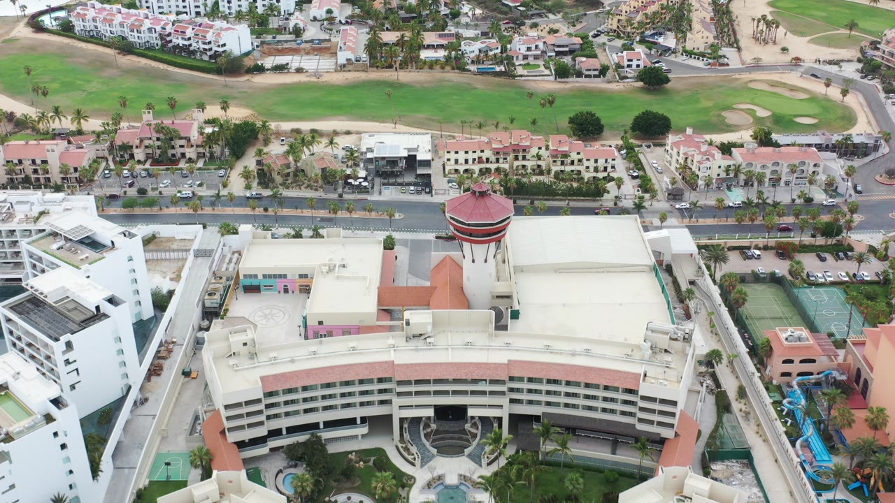 Aerial view of a large cream building with a red-roofed tower near roads and golf greens.
