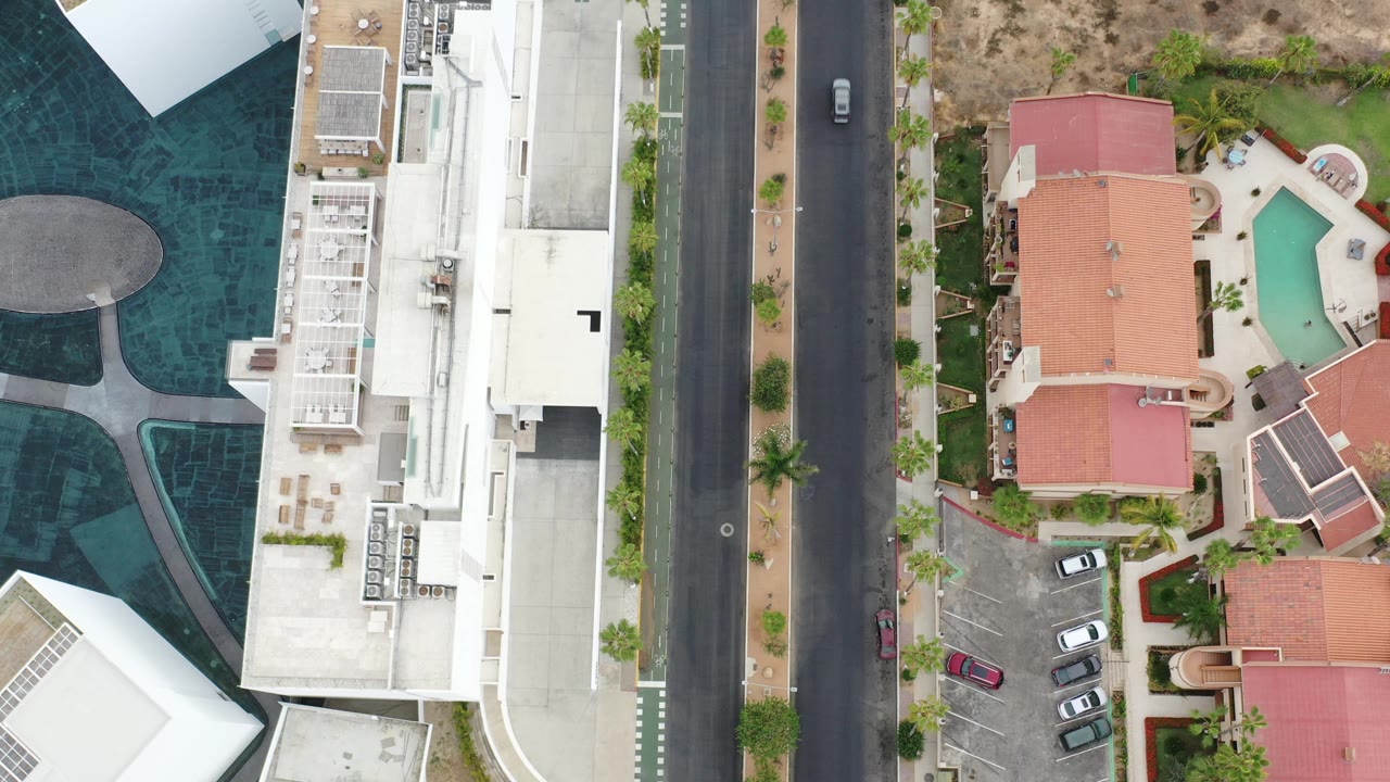 Top-down aerial view of a road between white buildings and red-roofed homes.