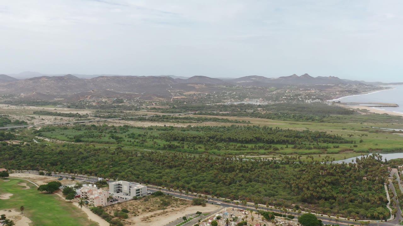 Aerial view of green lowlands, roads, buildings, hills, and coastline.