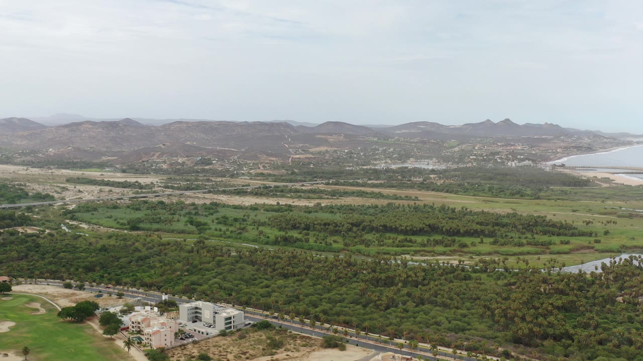 Wide aerial view of green land, roads, hills, and ocean horizon.