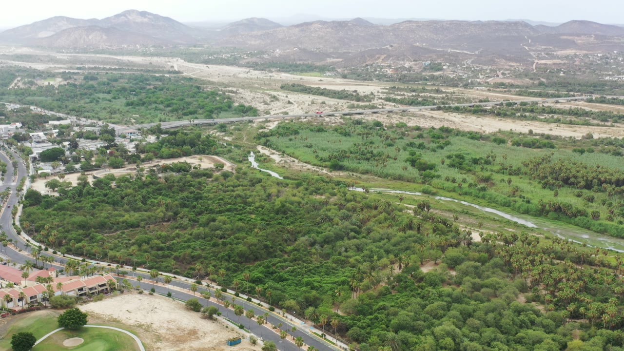 Aerial view of roads, red-roofed buildings, green vegetation, dry land, and distant hills.