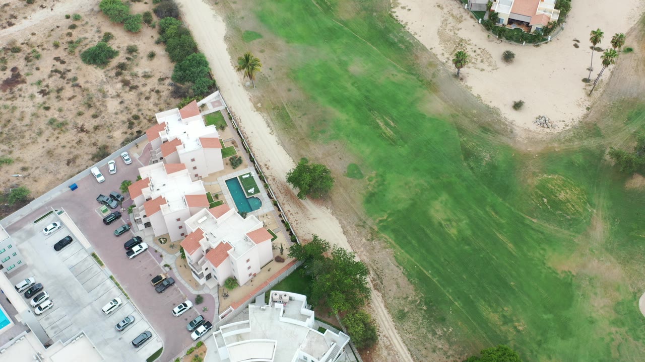 Top-down residential complex beside green grass and desert paths.