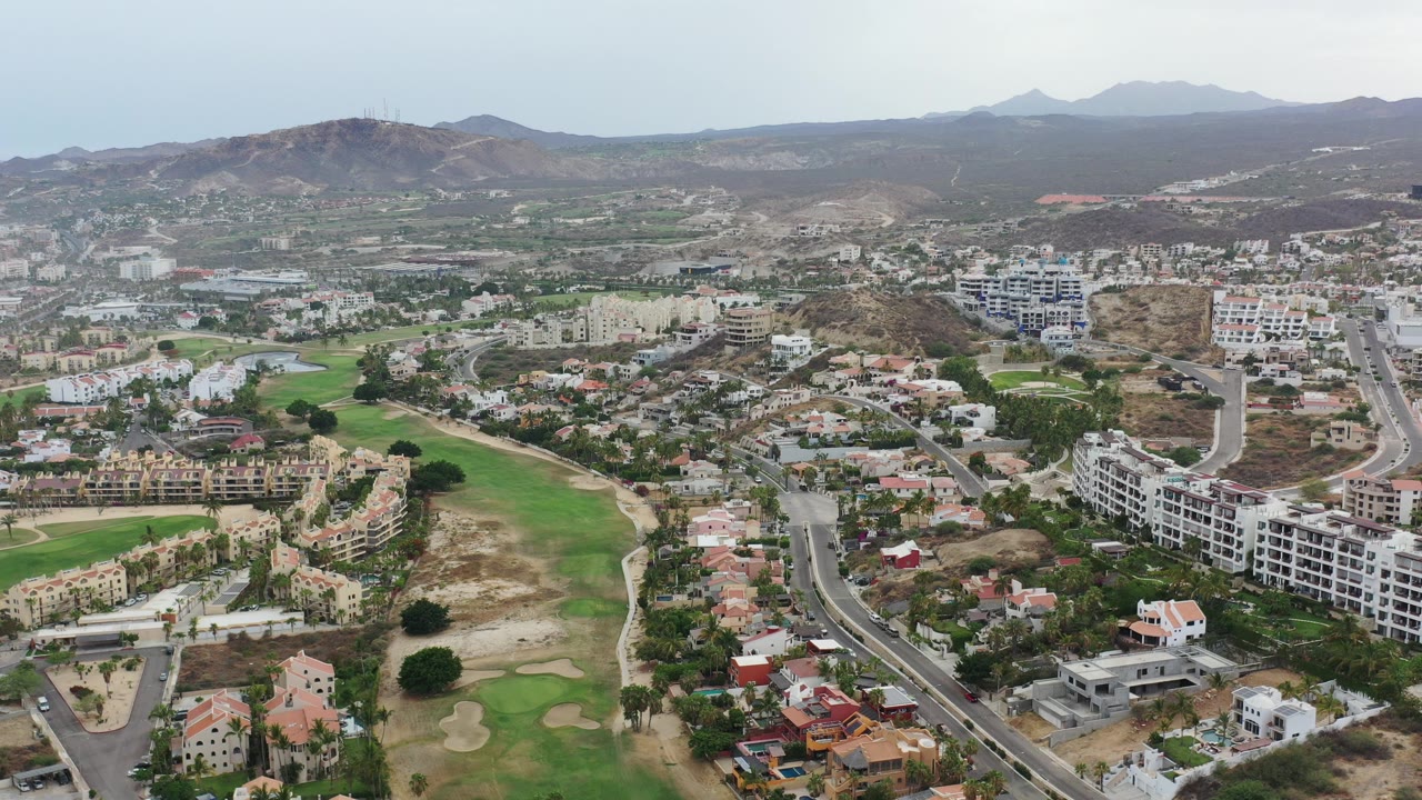 Aerial view of roads, homes, golf greens, and dry hills.