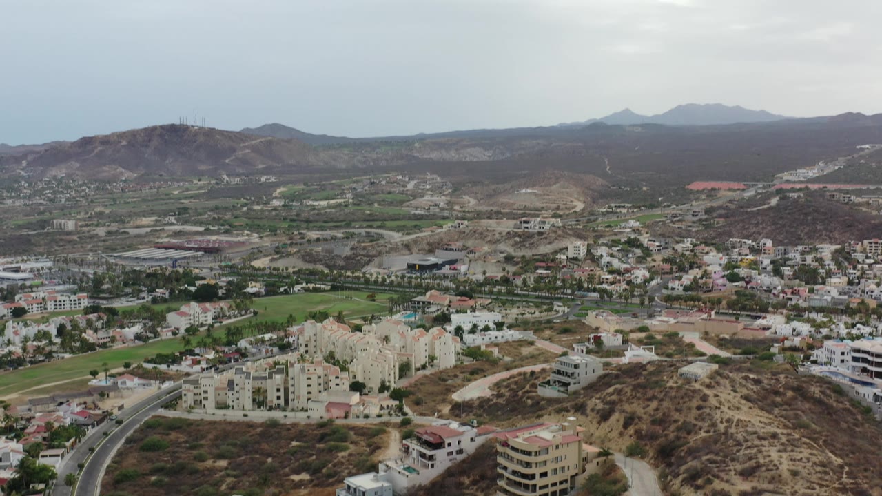 Elevated view of homes, winding roads, green lawns, dry hills, and mountain ridges.