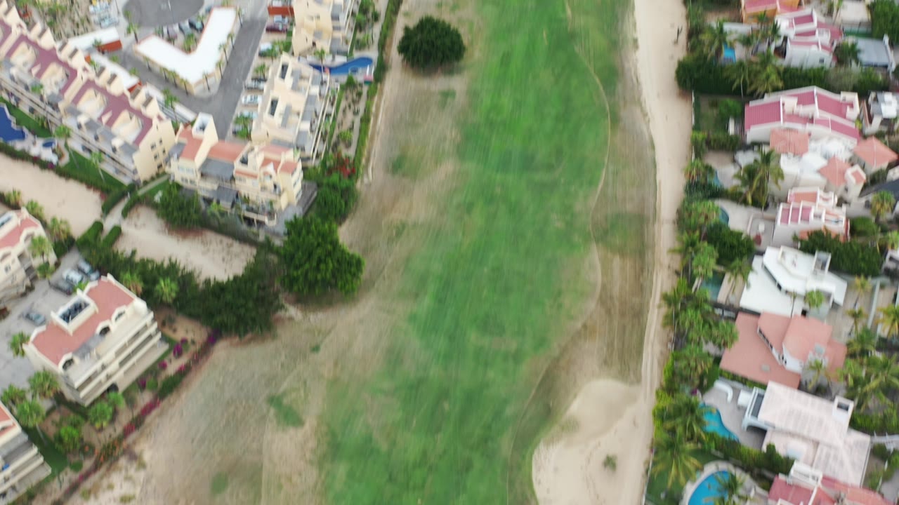 Overhead drone frame in Los Cabos showing private homes, red tile roofs, fairway grass, a sand bunker, and no visible people.