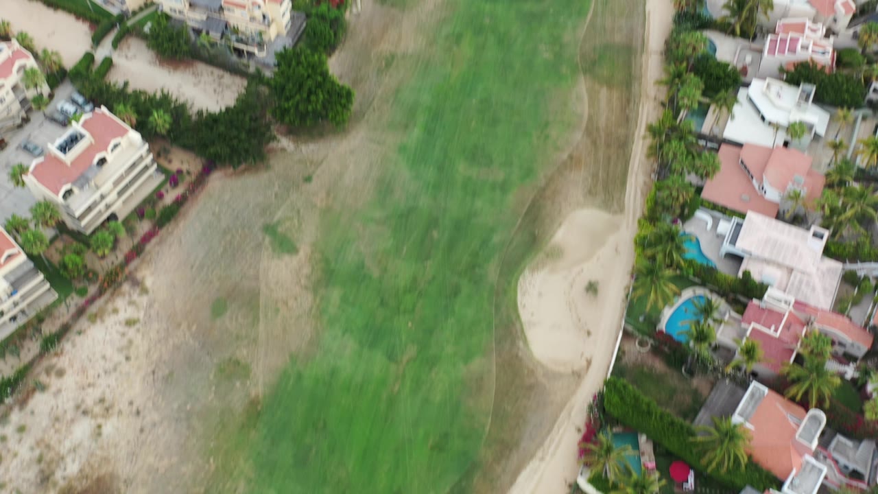 Top-down view of homes, palms, and golf-course grass near a sand trap.