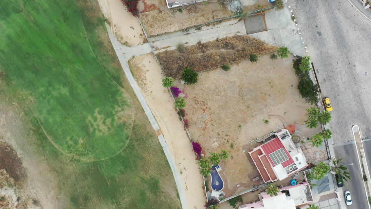 Top-down aerial view of homes, road, sandy lots, and green turf.