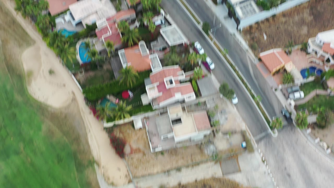 Overhead view of homes, road, green turf, and a sand-colored lot.