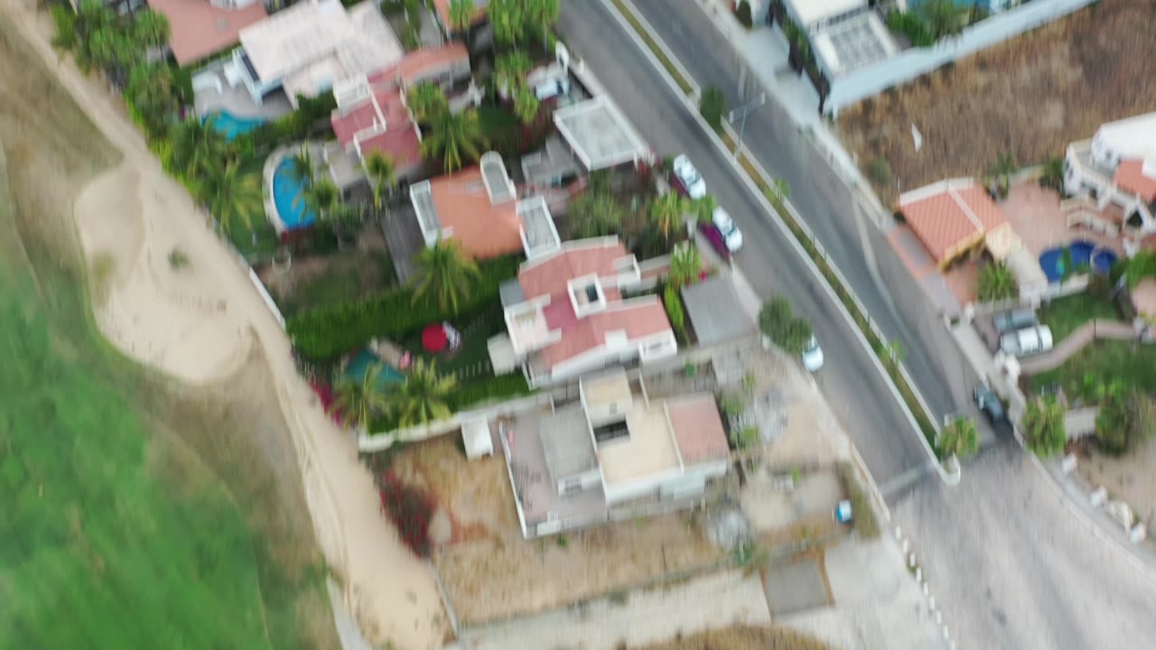Aerial view in Los Cabos, Mexico with white and red-roofed homes, small blue pools, roadside lots, dry ground, and no visible people.