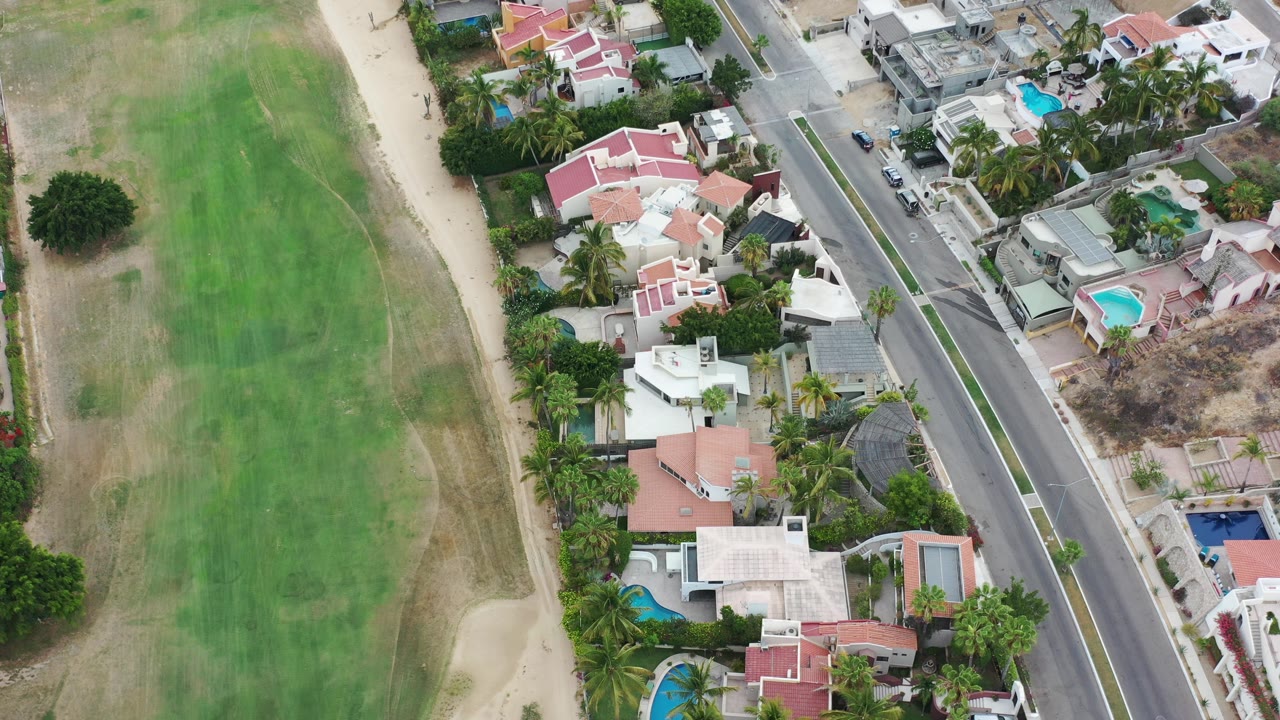 Overhead aerial view of golf fairway, sand path, houses, pools, and road.