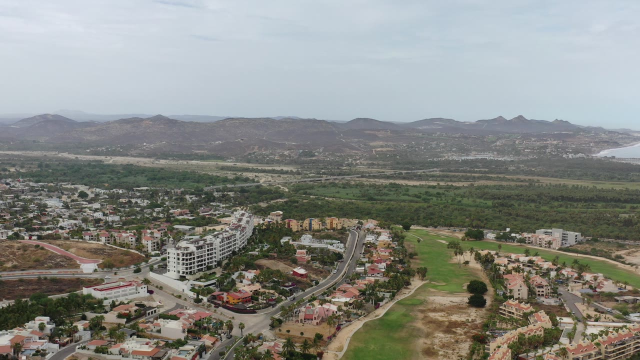 Aerial view of roads, homes, green land, hills, and distant coastline.