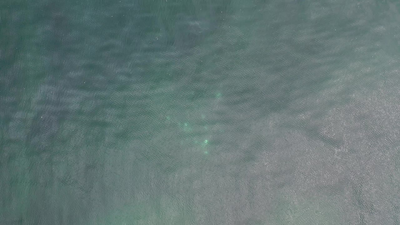 Overhead ocean surface in Los Cabos, Mexico, showing faint brighter aqua patches beneath gray-green ripples and no visible people.