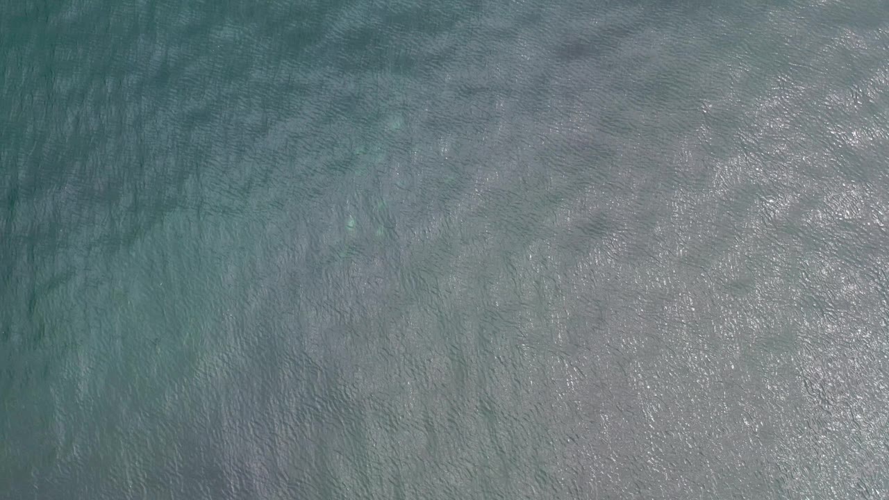 Blue-green ocean surface in Los Cabos, Mexico, with darker underwater bands and scattered bright highlights, with no visible people.
