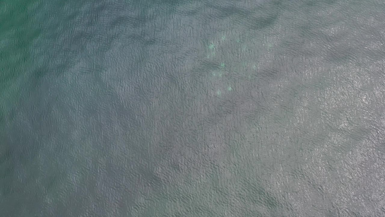 Aerial view of softly rippled Los Cabos sea water, where pale submerged areas spread through gray-blue surface texture with no visible people.