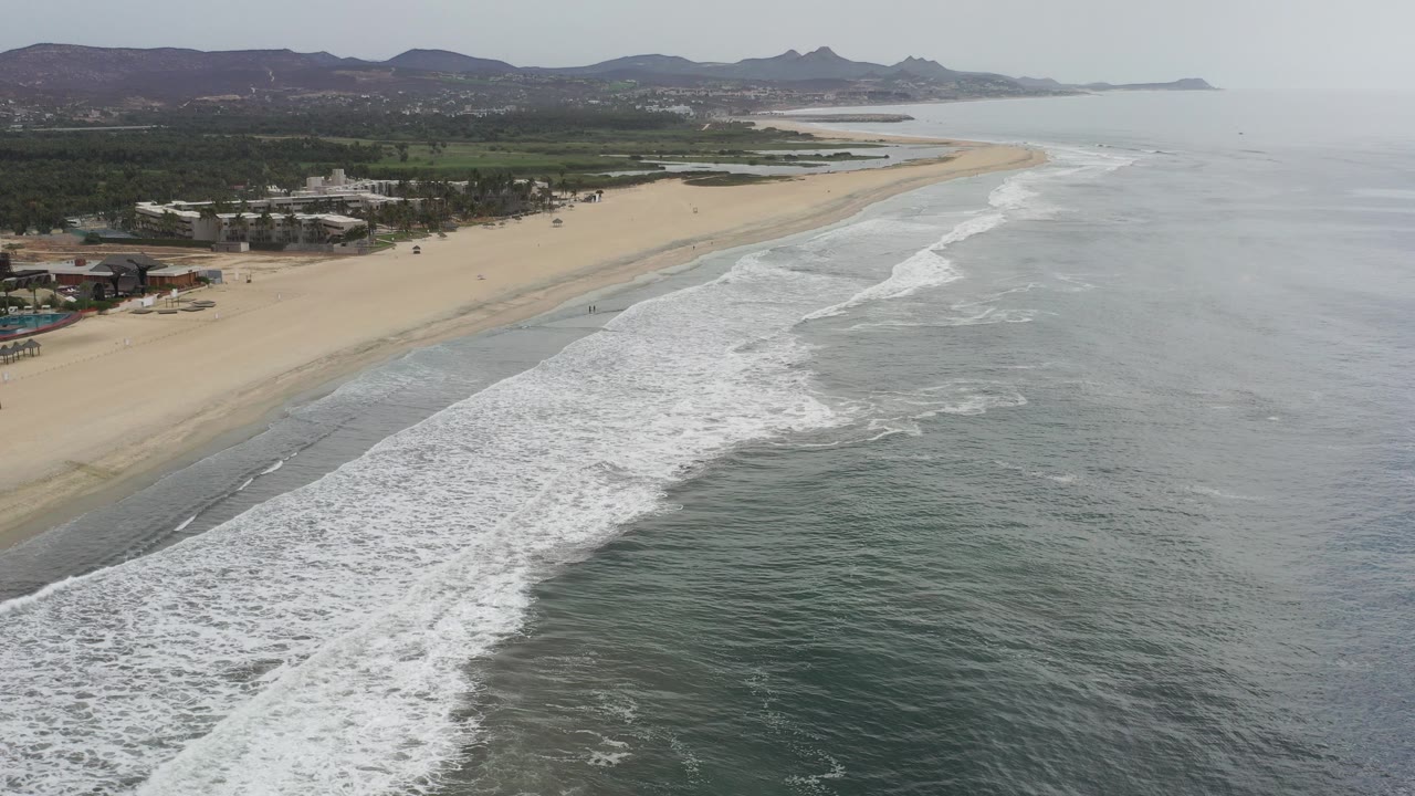 Aerial view of beach, surf, oceanfront buildings, and distant mountains.