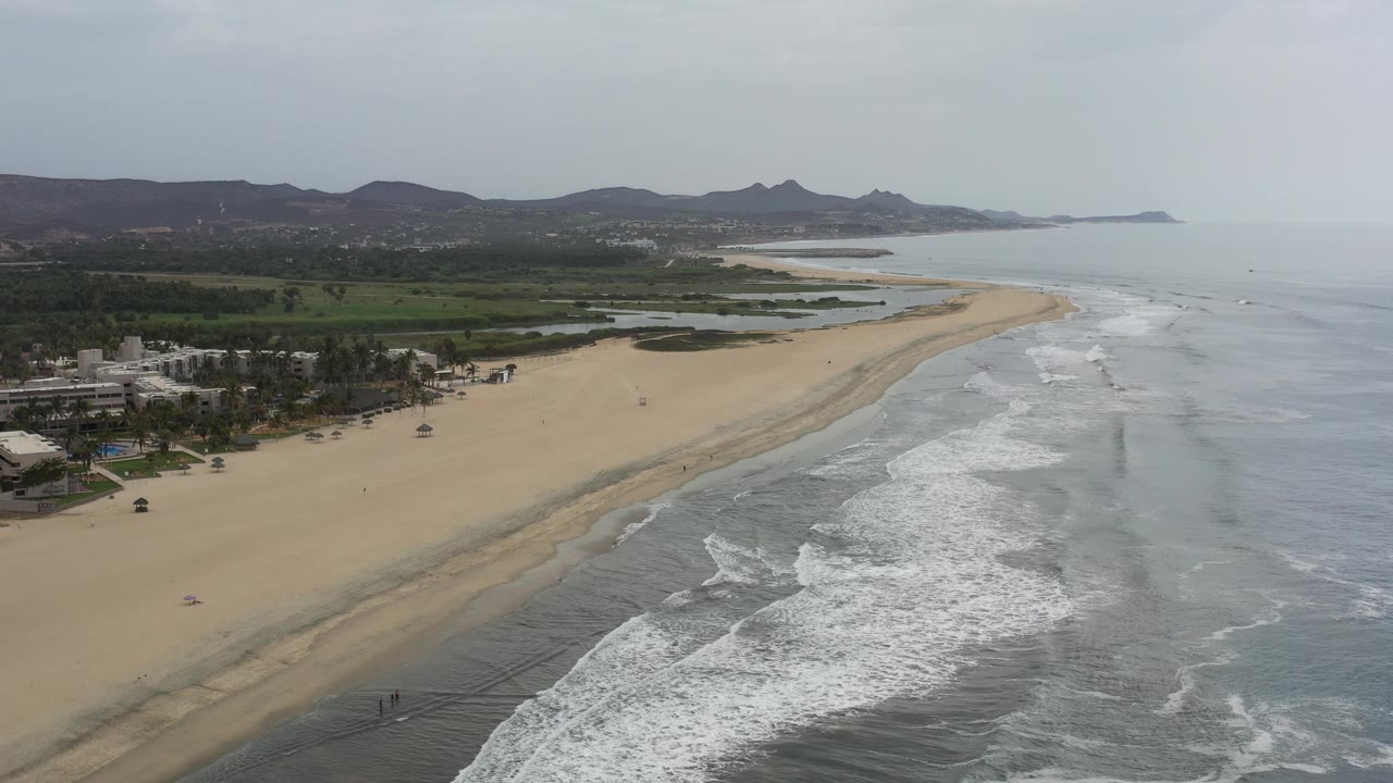 Drone view of empty beach, surf bands, and low mountains beyond the coast.