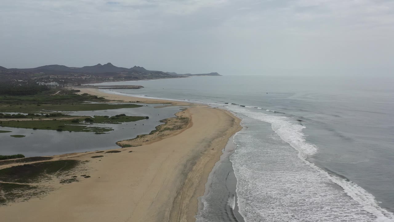 Beach and ocean aerial with surf lines, lagoon water, and mountain background