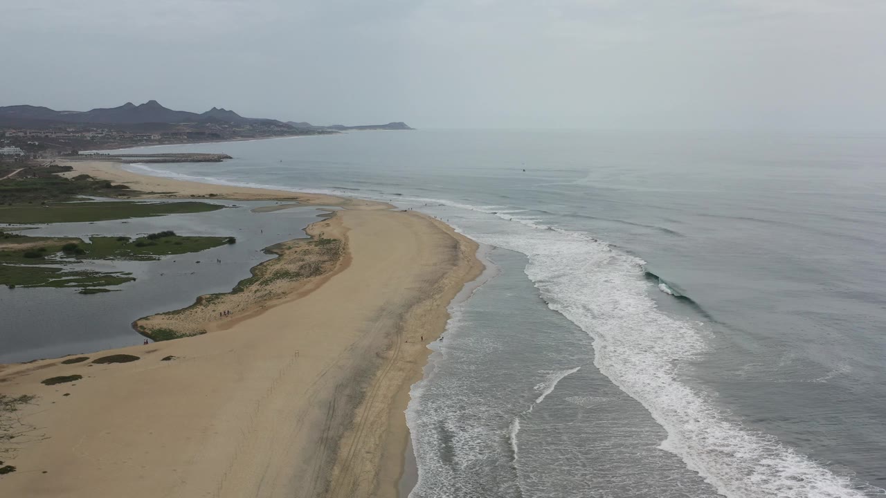Drone-like view down a beach with waves breaking along the shore.