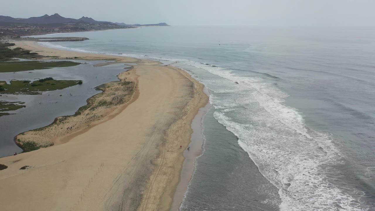 Coastline aerial with sandbar, surf, and distant hills.