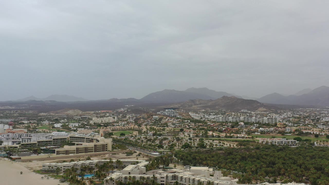 Aerial view of town buildings, trees, and hills under a gray sky.