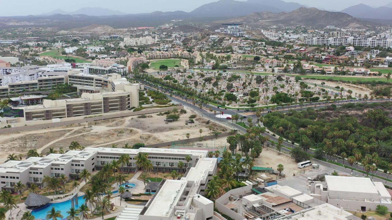 Aerial view over white buildings, pools, road, and hills.