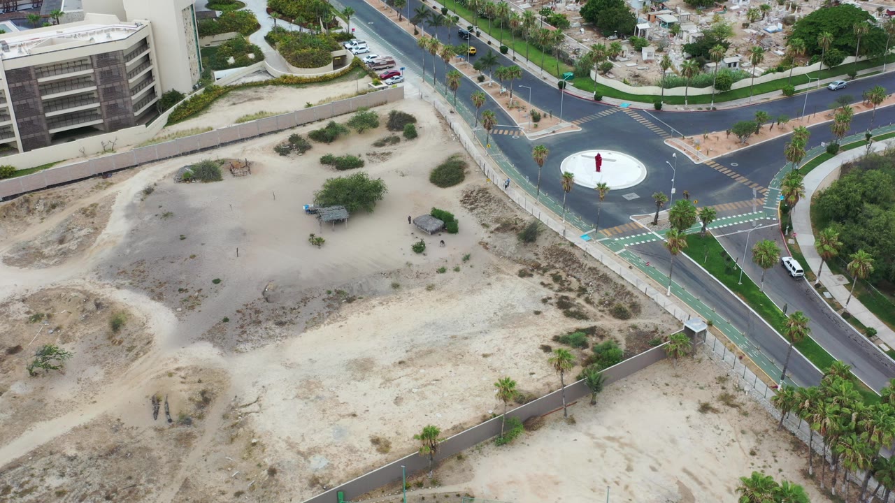 Top-down aerial view of a roundabout beside sandy lots and modern buildings.