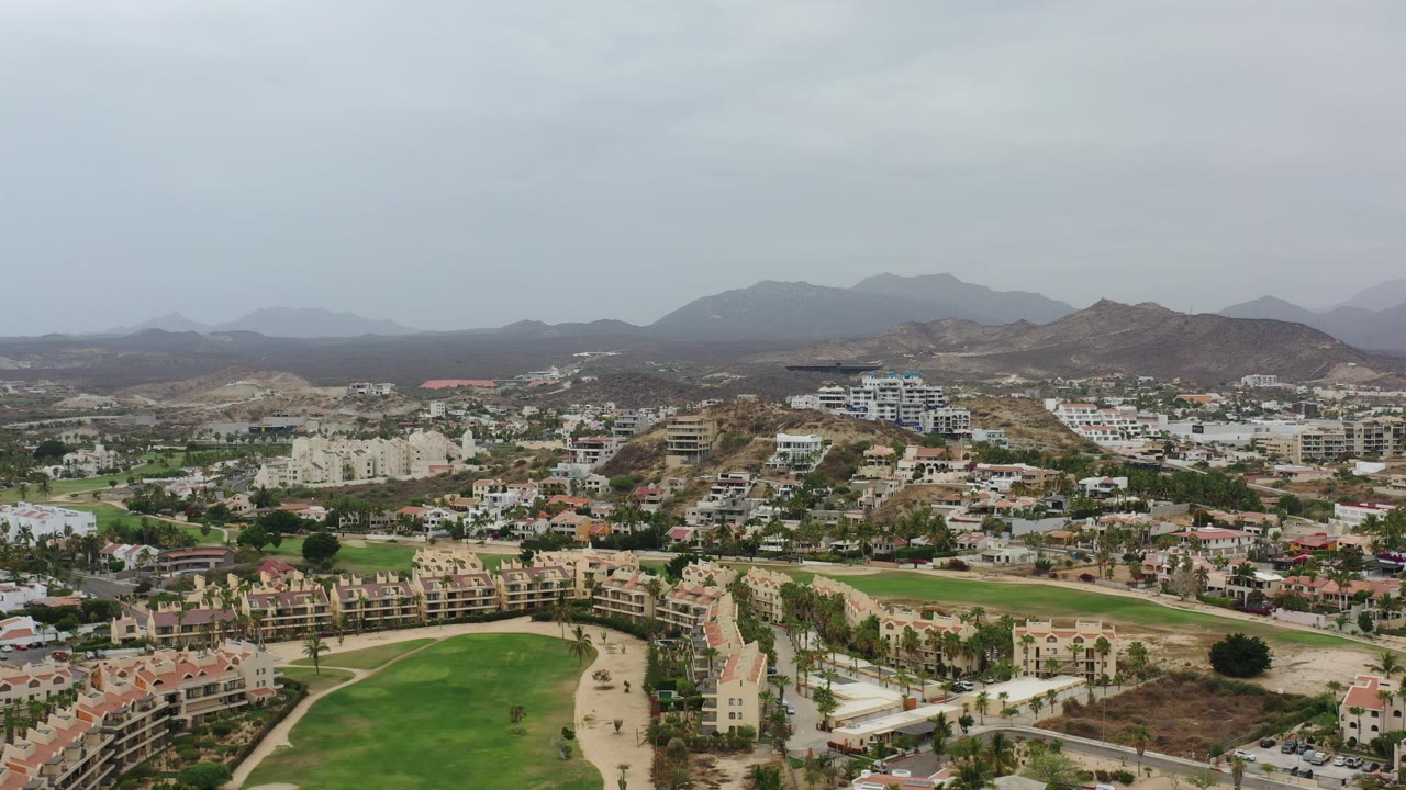 Aerial view of residential buildings, green lawns, roads, hills, and distant mountains.